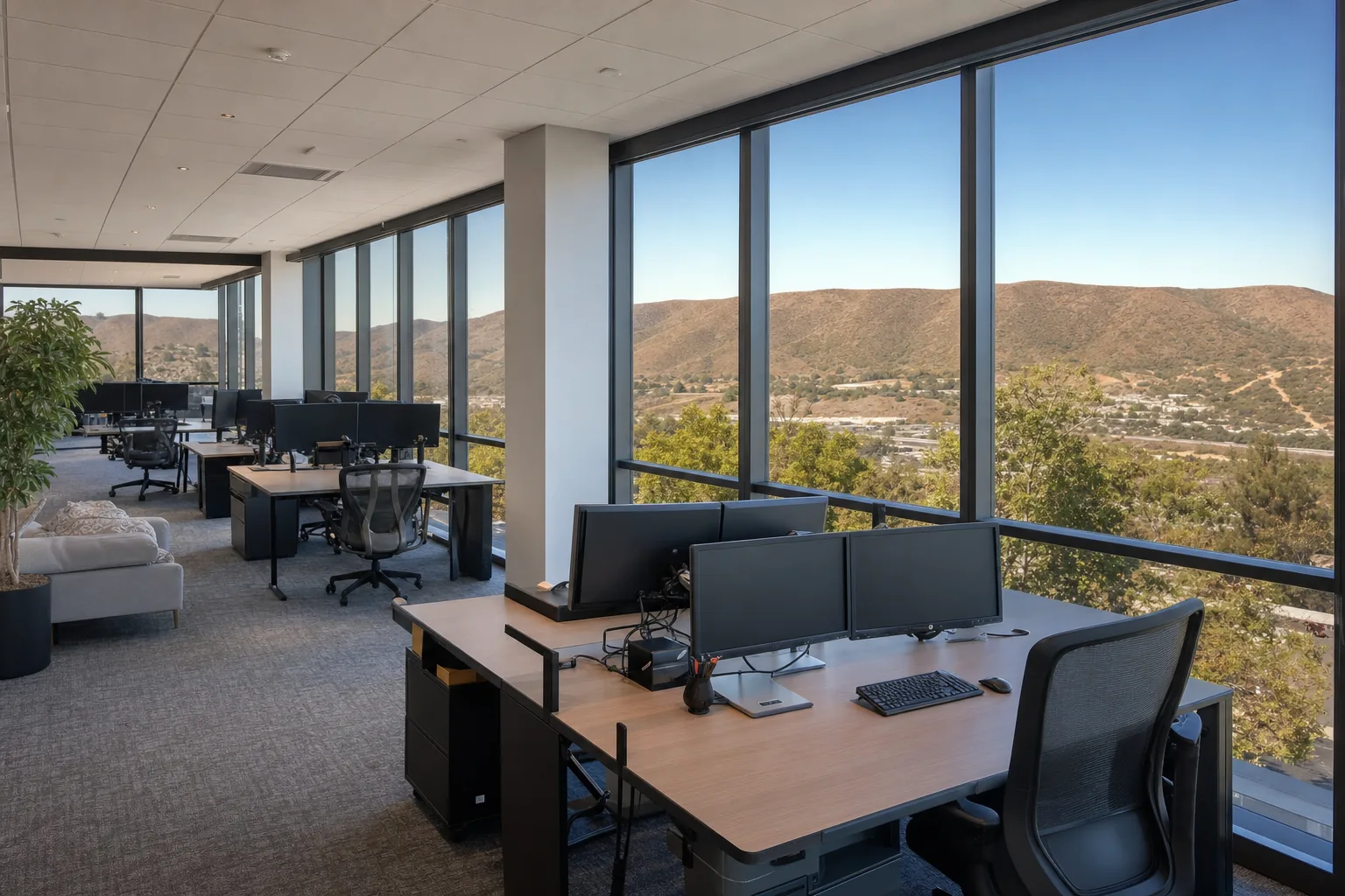 An open-plan office with glare-free screens beside filmed floor-to-ceiling windows