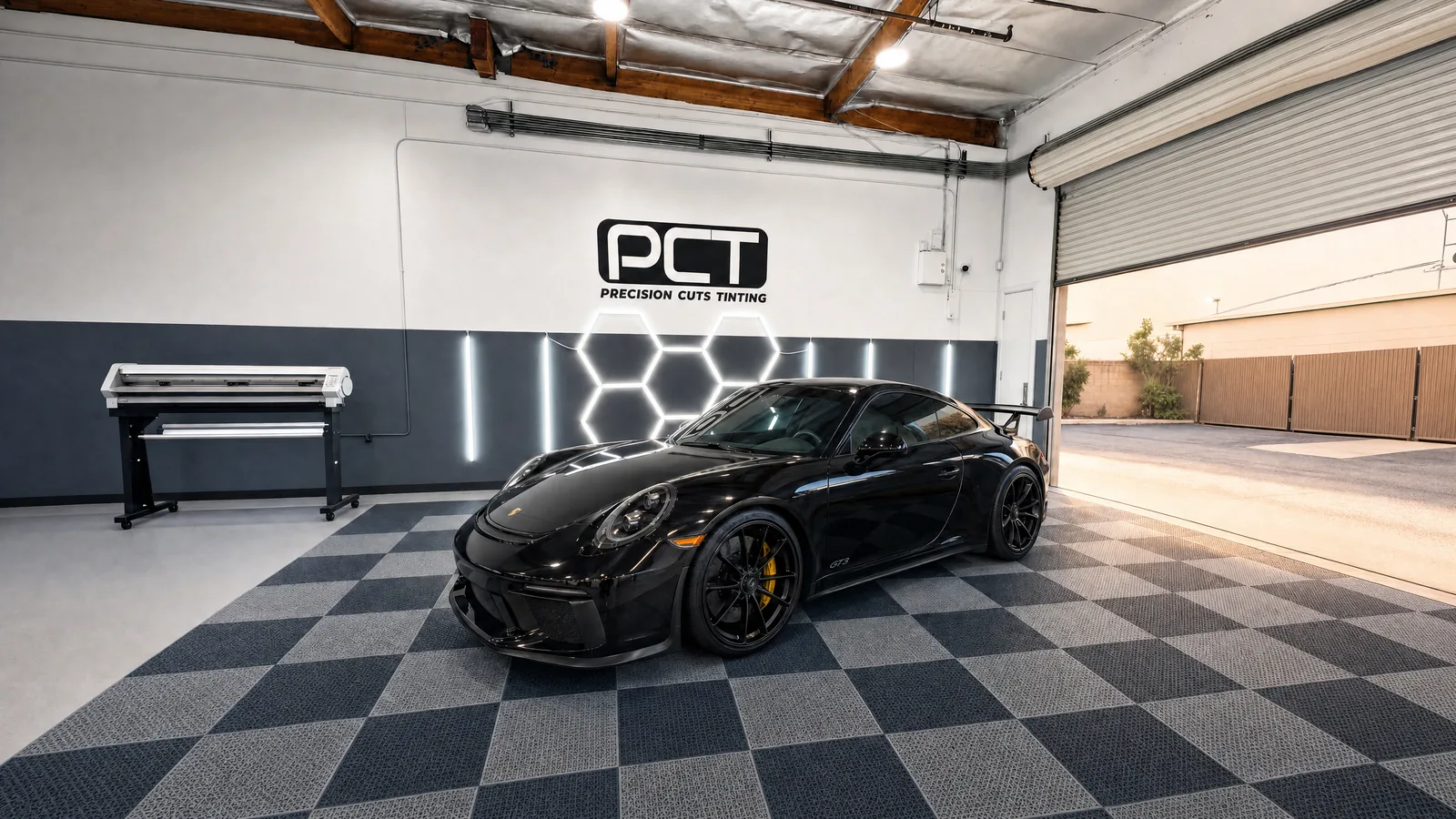 A black Porsche 911 GT3 in the Precision Cuts Tinting studio at the end of the day, the roller door half open